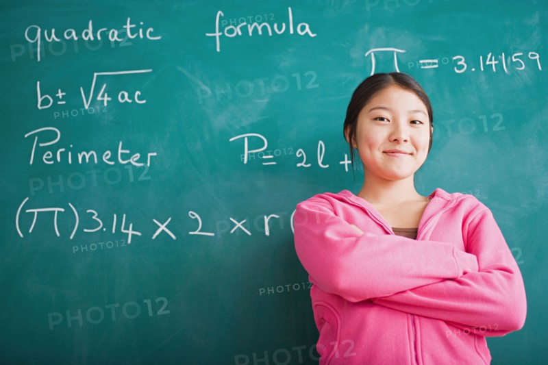 Happy Asian girl standing against blackboard after solving mathematical equation. Photo : Rob Lewine