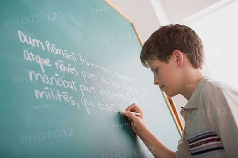 Boy writing Latin text on blackboard. Photo : Rob Lewine