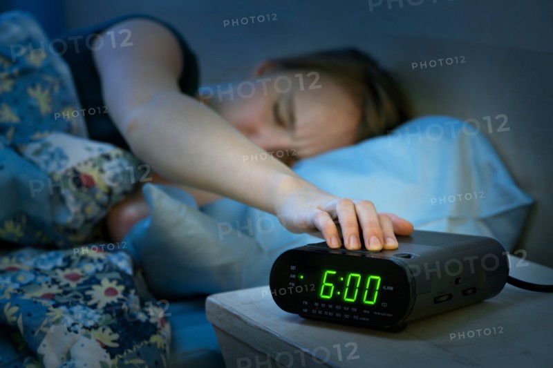 Teenage girl with hand on alarm clock. Photo : Elena Elisseeva