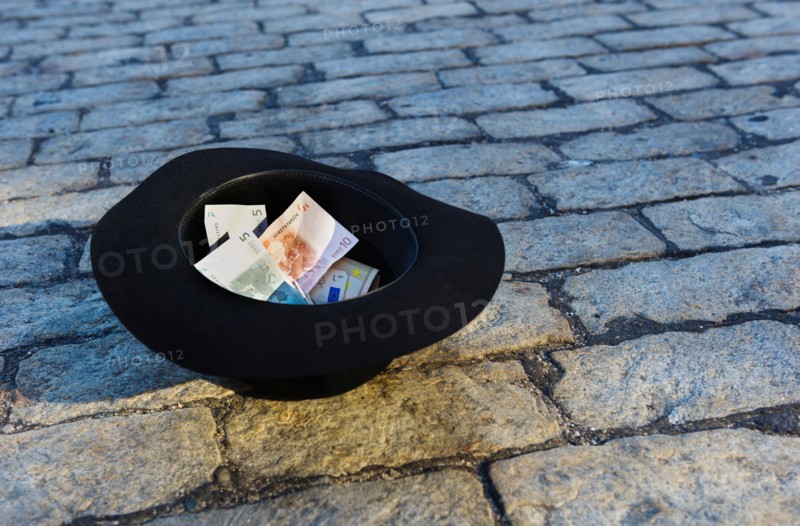 Money in hat on cobblestone street.