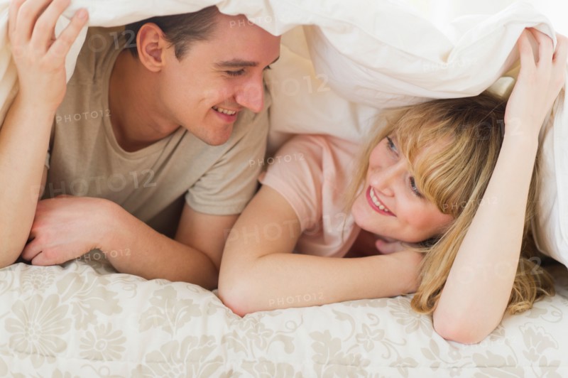 Couple lying on bed under duvet.