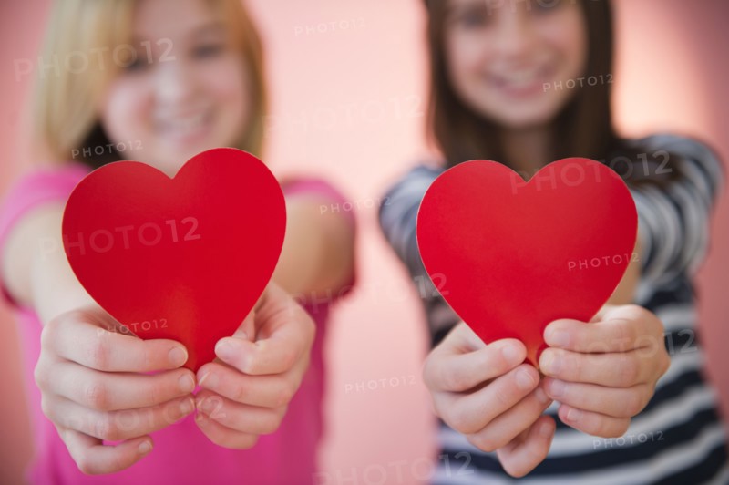 Close up of two girl's hands holding red hearts. Photo : Jamie Grill
