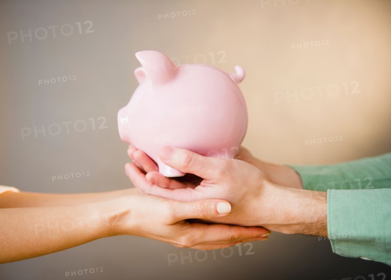 Close up of man's and woman's hands holding piggy bank, studio shot. Photo : Jamie Grill