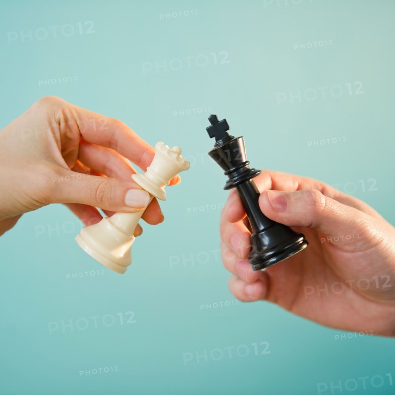Close up of man's and woman's hands holding chess pieces,  studio shot. Photo : Jamie Grill