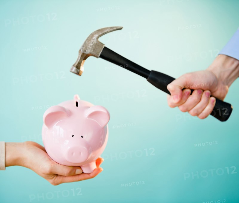 Close up of man's and woman's hands holding piggy bank and hammer,  studio shot. Photo : Jamie Grill