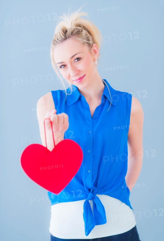 Portrait of smiling young woman holding red heart, studio shot. Photo : Daniel Grill