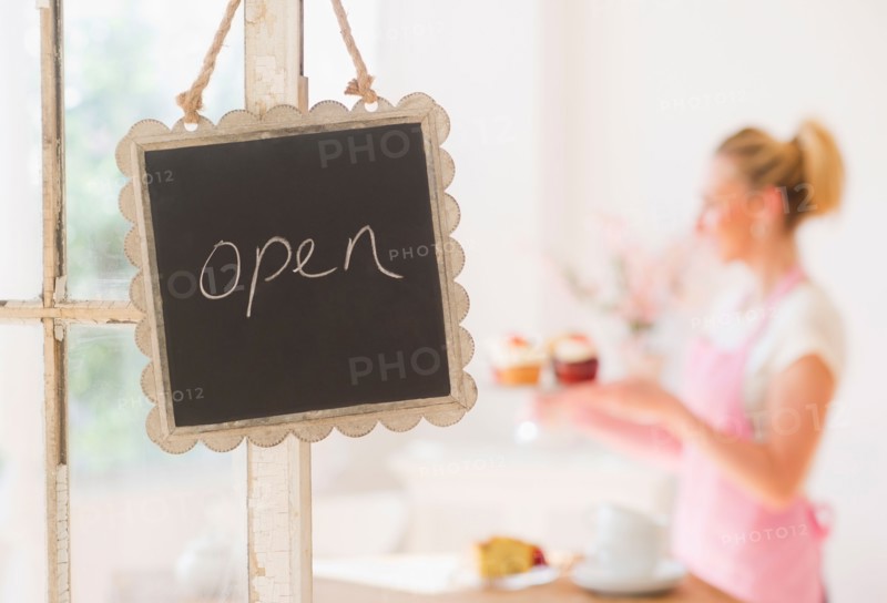 Close up of open sign with woman in background. Photo : Daniel Grill