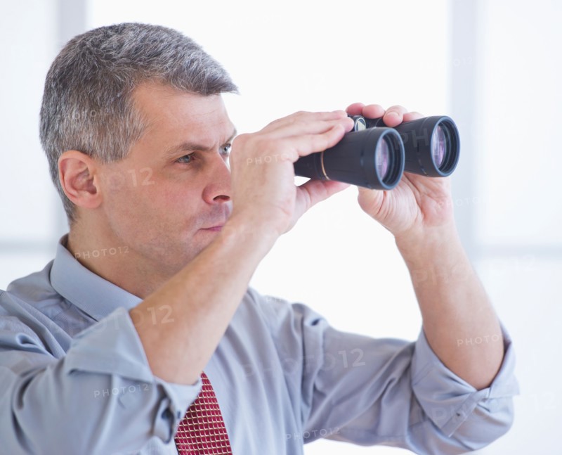 Portrait of businessman holding binoculars. Photo : Daniel Grill