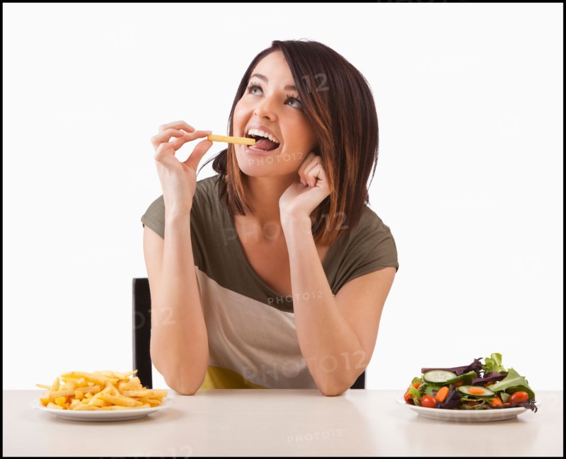 Young woman choosing between healthy and unhealthy food. Photo : Mike Kemp