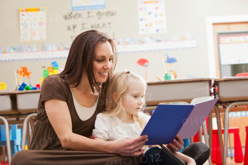 Teacher with girl (4-5) reading book. Photo : Mike Kemp