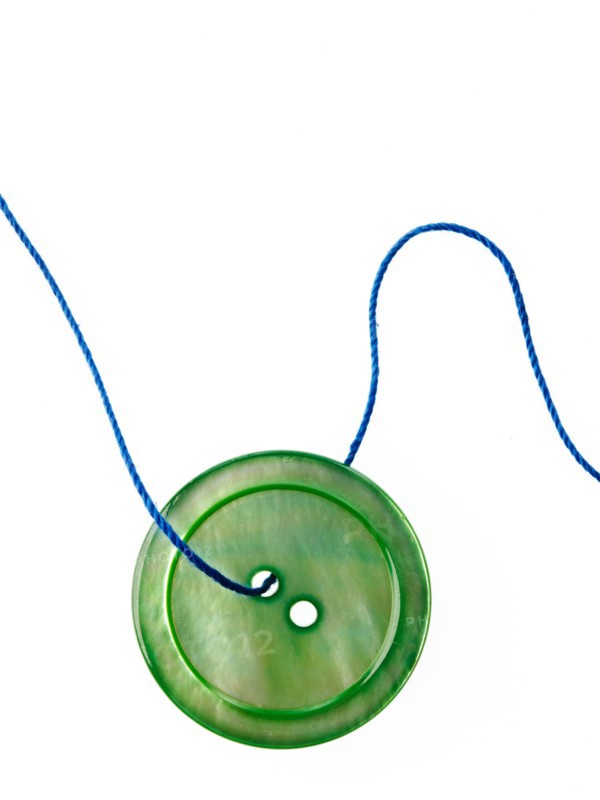 Studio shot of single green button on thread. Photo : David Arky