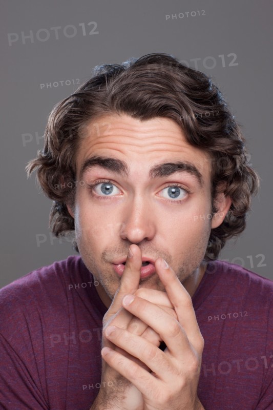 Studio shot of young man with finger on his lips. Photo : Rob Lewine
