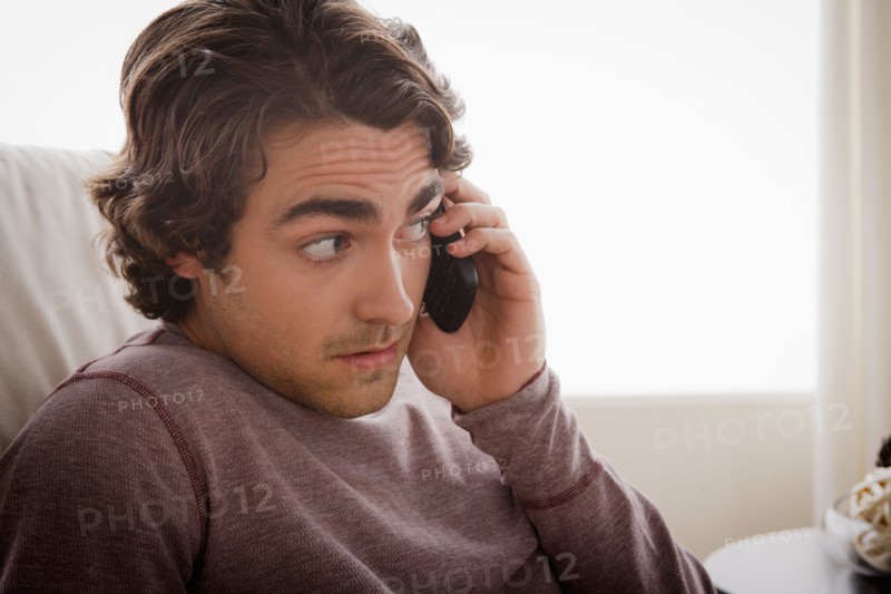 Young man sitting on armchair and talking via mobile. Photo : Rob Lewine