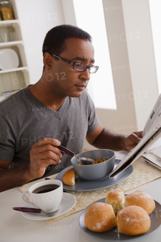 Mature man eating breakfast and reading newspaper. Photo : Rob Lewine