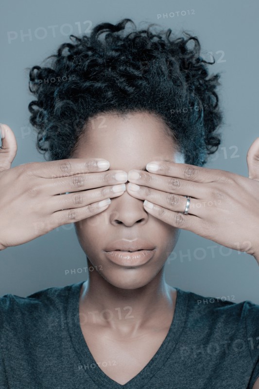 Studio shot of young woman with hands covering eyes. Photo : Rob Lewine