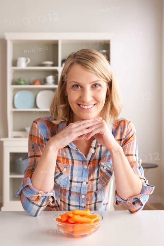 Portrait of mid adult woman with bowl of carrots. Photo : Rob Lewine