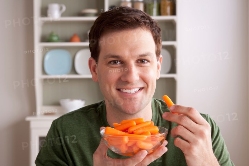 Portrait of mid adult man with bowl of carrots. Photo : Rob Lewine