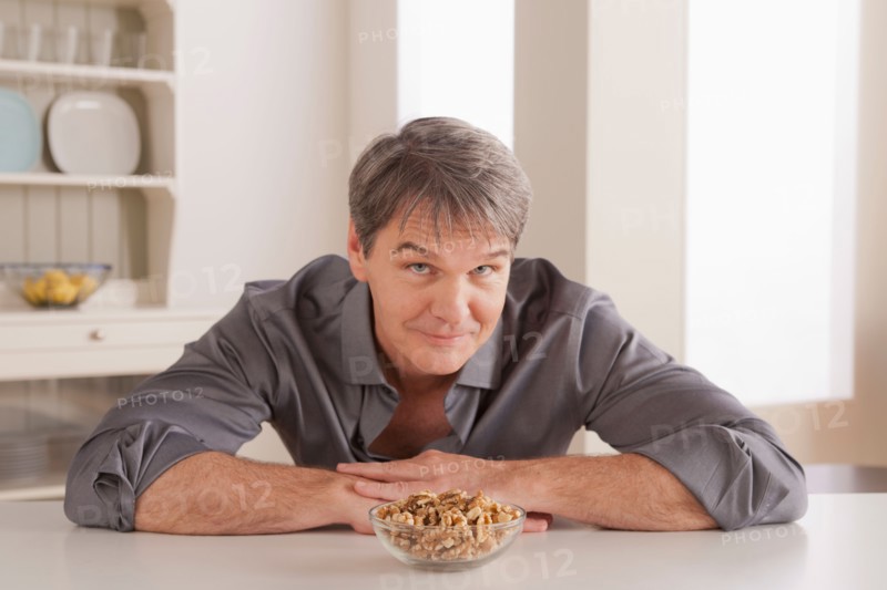 Portrait of mature man with snacks on table. Photo : Rob Lewine