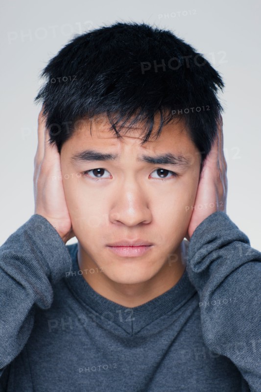 Studio portrait of young man covering ears. Photo : Rob Lewine