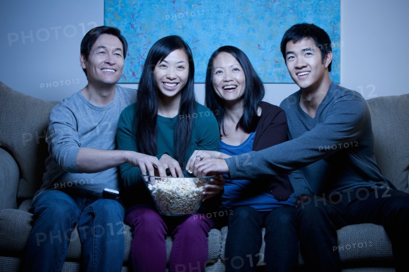 Smiling family watching TV and eating popcorn. Photo : Rob Lewine