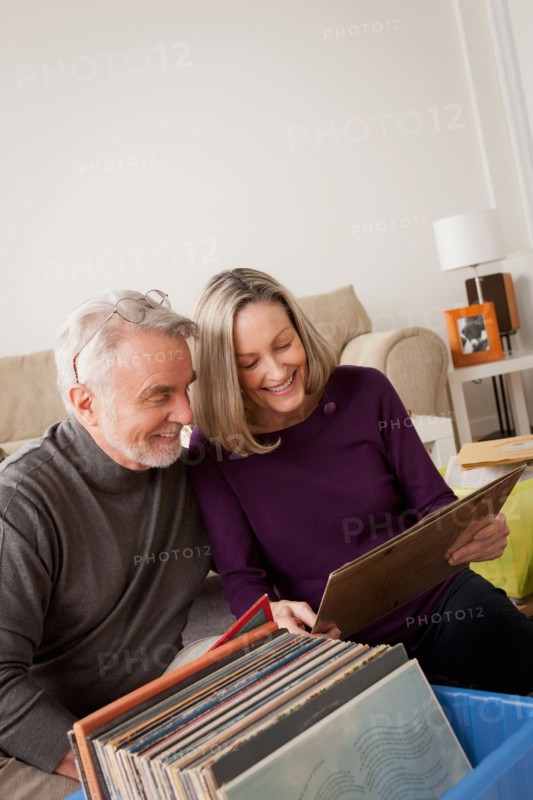 Smiling senior couple looking at vinyl's in living room. Photo : Rob Lewine