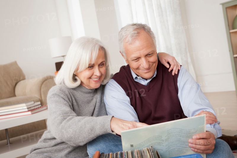 Smiling senior couple looking at vinyl's in living room. Photo : Rob Lewine