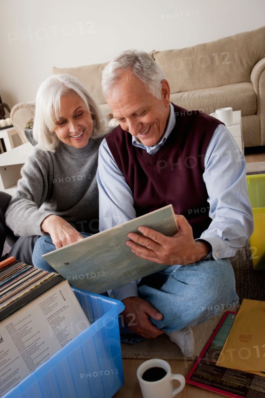 Smiling senior couple looking at vinyl's in living room. Photo : Rob Lewine