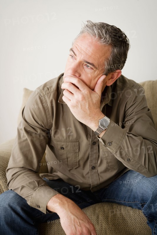 Worried mature man sitting on sofa. Photo : Rob Lewine