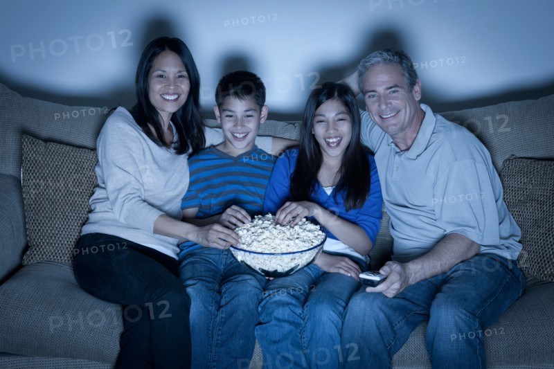 Family sitting on sofa and watching television. Photo : Rob Lewine