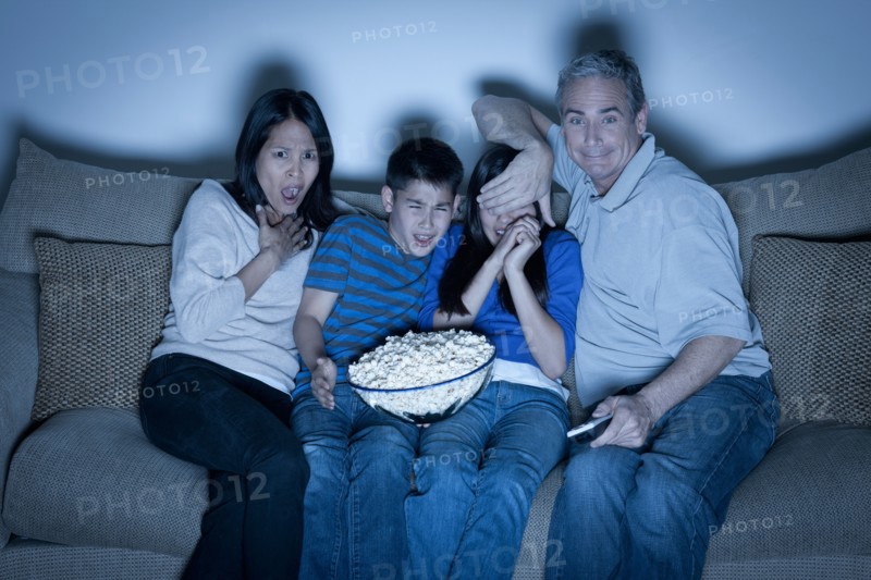 Family sitting on sofa and watching television. Photo : Rob Lewine