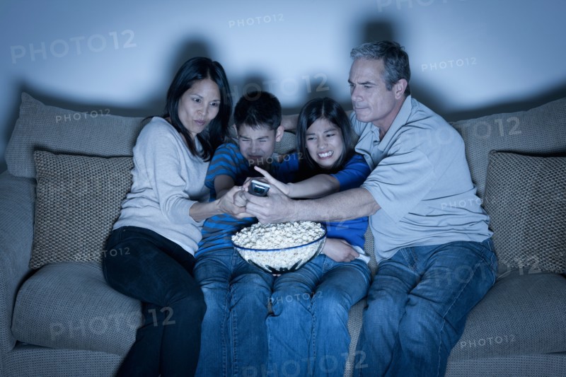 Family sitting on sofa and watching television. Photo : Rob Lewine