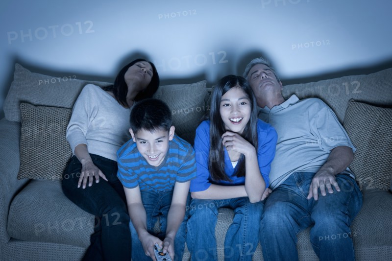 Family sitting on sofa and watching television. Photo : Rob Lewine