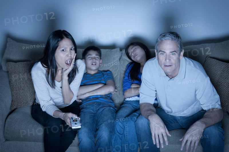 Family sitting on sofa and watching television. Photo : Rob Lewine