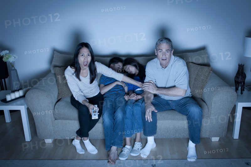 Family sitting on sofa and watching television. Photo : Rob Lewine