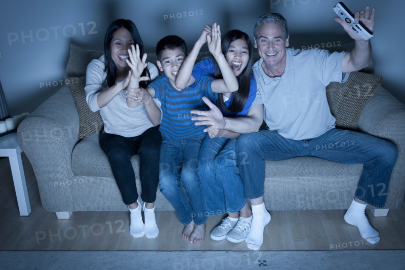 Family sitting on sofa and watching television. Photo : Rob Lewine