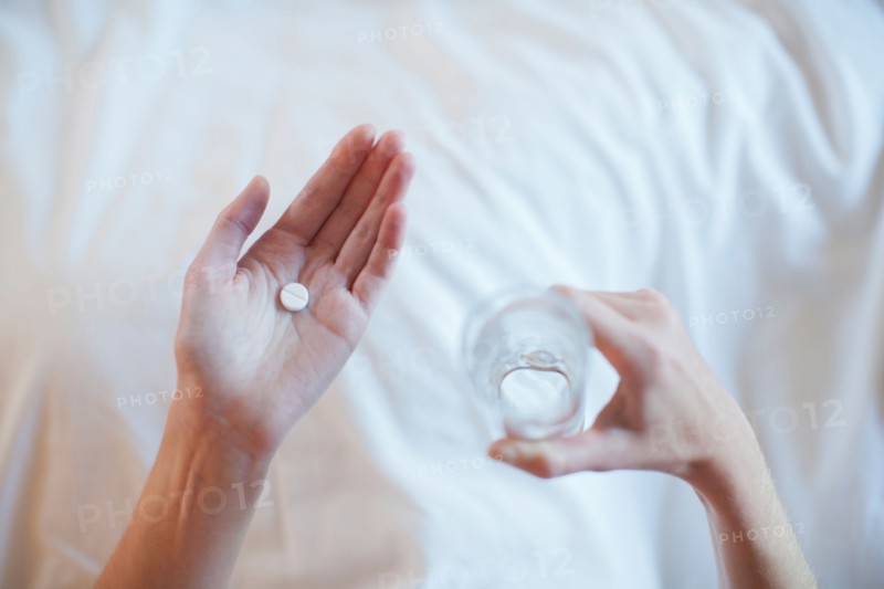 Young woman taking medicine while lying in bed . Photo : Mark de Leeuw
