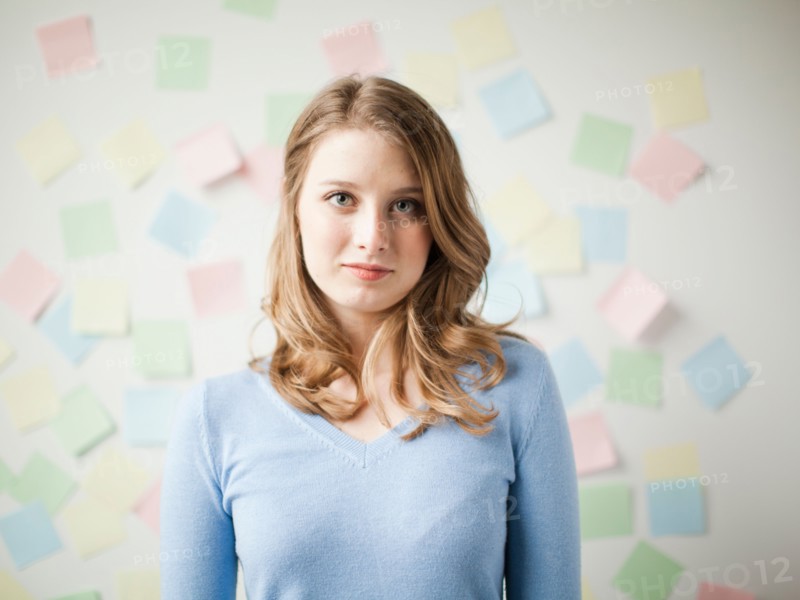 Indoor portrait of young attractive woman standing in f front of wall covered in adhesive notes. Photo : Jessica Peterson