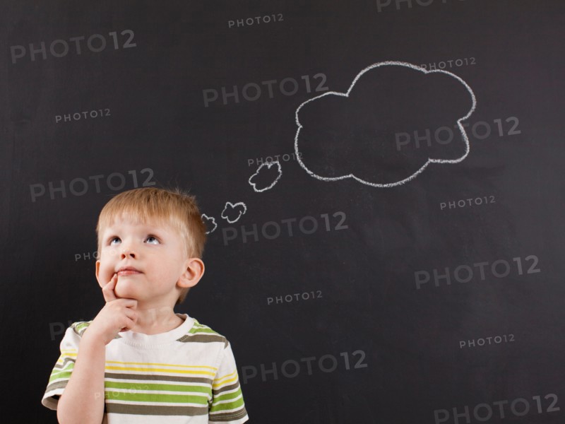Cute toddler boy (2-3) standing against blackboard with thought bubble written in chalk. Photo : Jessica Peterson