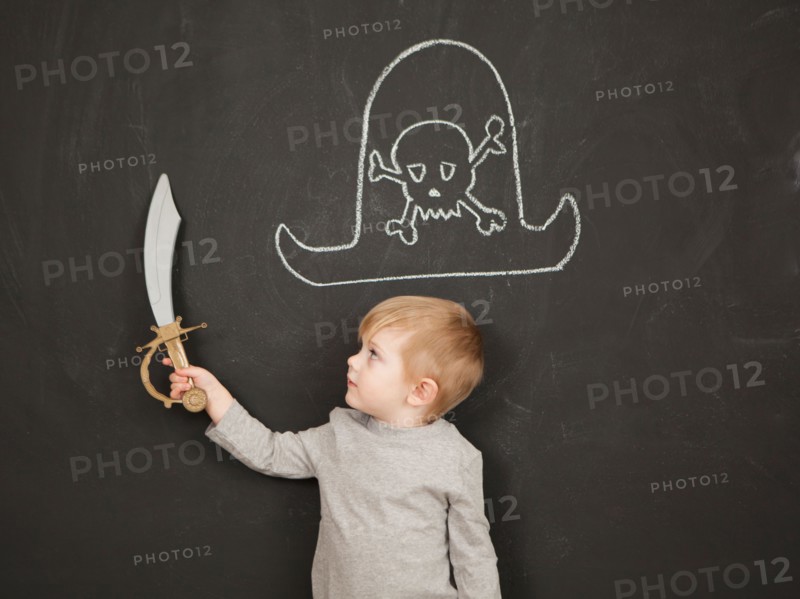 Cute toddler boy (2-3) standing against blackboard posing as pirate. Photo : Jessica Peterson