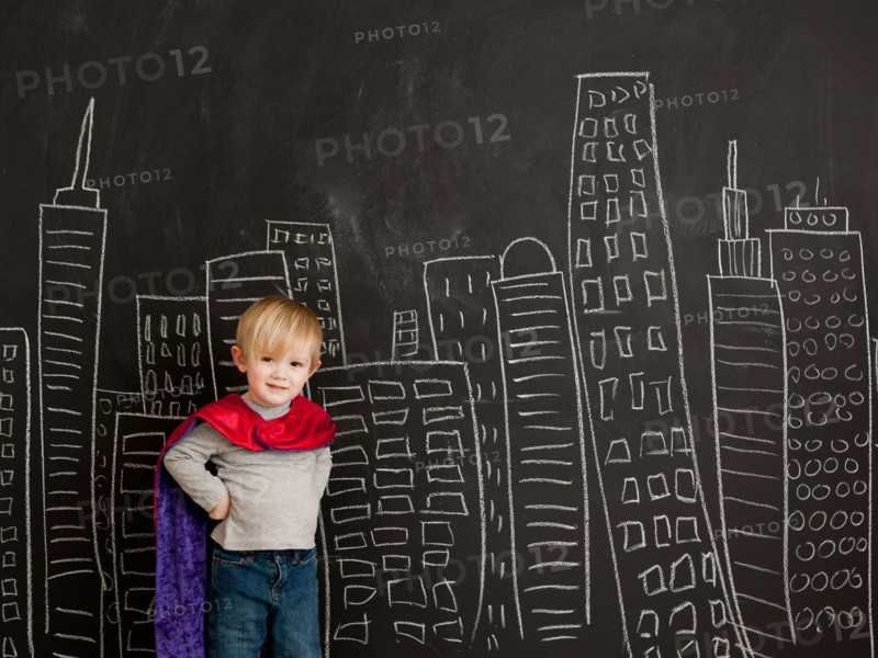 Cute toddler boy (2-3) standing against blackboard with city skyline drawn on it. Photo : Jessica Peterson