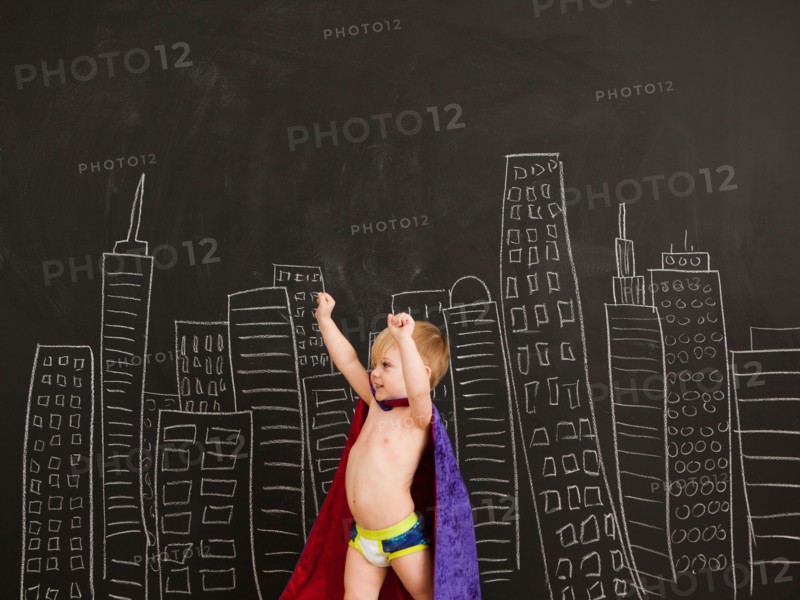Cute toddler boy (2-3) standing against blackboard with city skyline drawn on it. Photo : Jessica Peterson