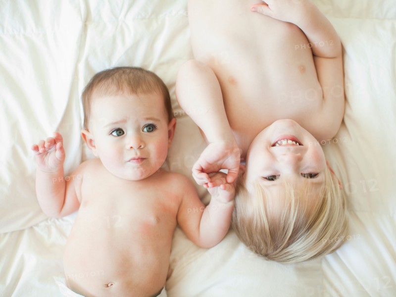 Toddler boy (2-3) lying in bed with baby sister (6-11 months). Photo : Jessica Peterson