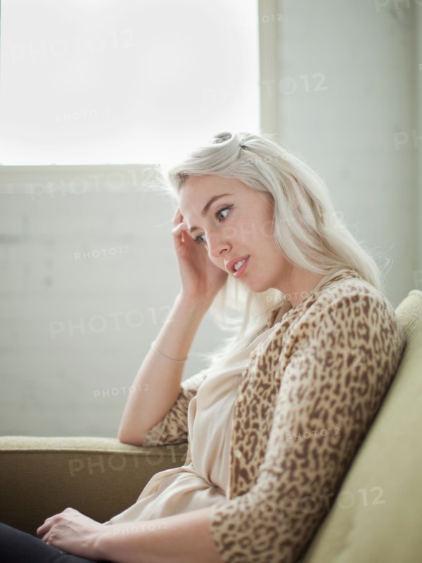 Thoughtful young woman sitting on sofa. Photo : Jessica Peterson