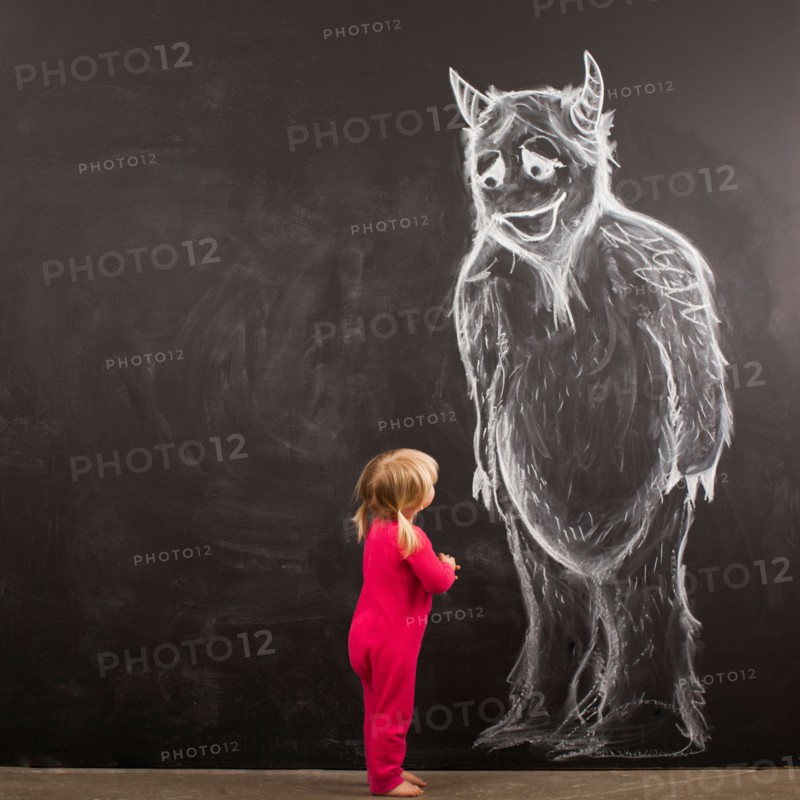 Portrait of baby girl (18-23 months) in front of huge monster drawn on blackboard. Photo : Jessica Peterson