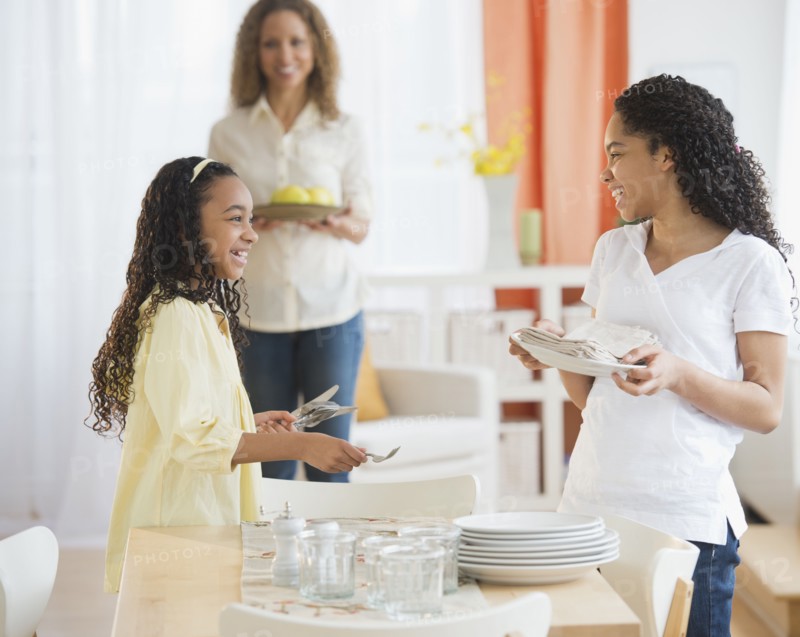 Mother with daughters (10-13) setting table.