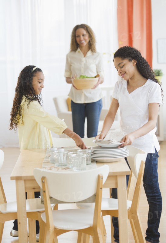 Mother with daughters (10-13) setting table.