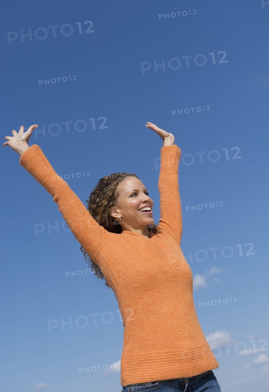 Mature woman with arms raised towards blue sky.