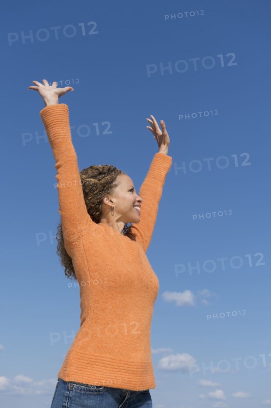 Mature woman with arms raised towards blue sky.