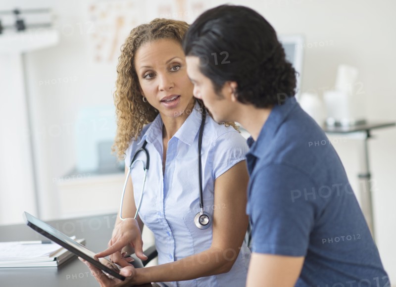 Doctor and patient talking in clinic using tablet pc.