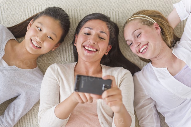 Friends (14-19) lying on floor looking at mobile phone.